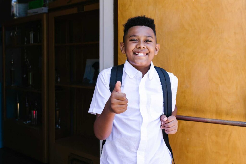 A young student going to school giving thumbs up